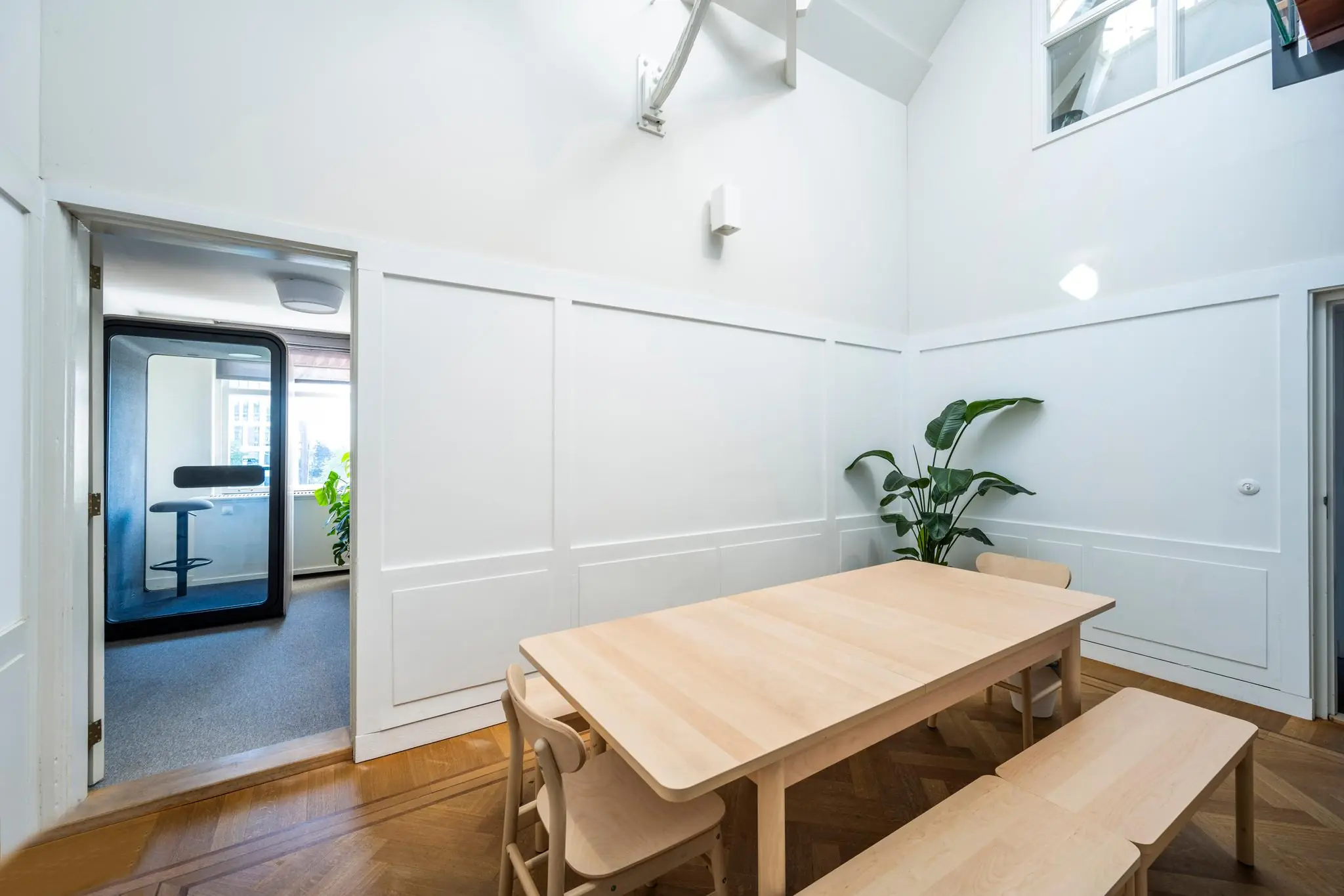 Licht ingerichte vergaderruimte aan de Prof. Tulpstraat met houten tafel, stoelen en een akoestische belcel in de aangrenzende kamer.